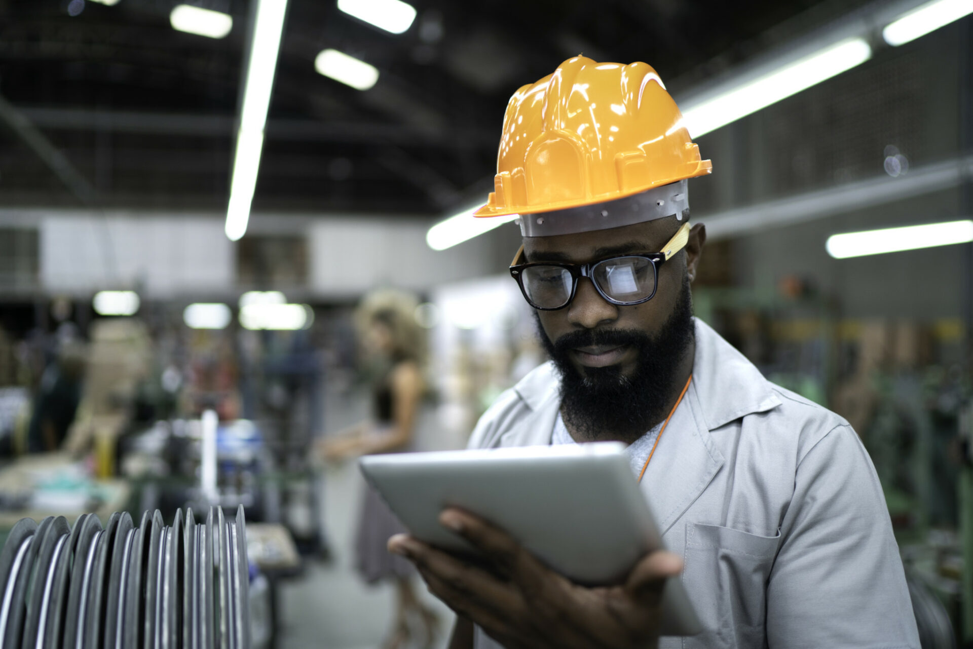 A man wearing a hardhat reviews information on a tablet while in a factory.
